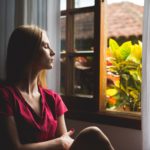 woman sitting by open window with eyes closed