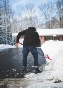 man shoveling snow from driveway in front of house